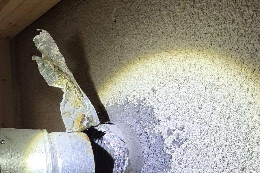 Water heater vent connector pushed into a chimney opening sealed with spray foam and foil tape